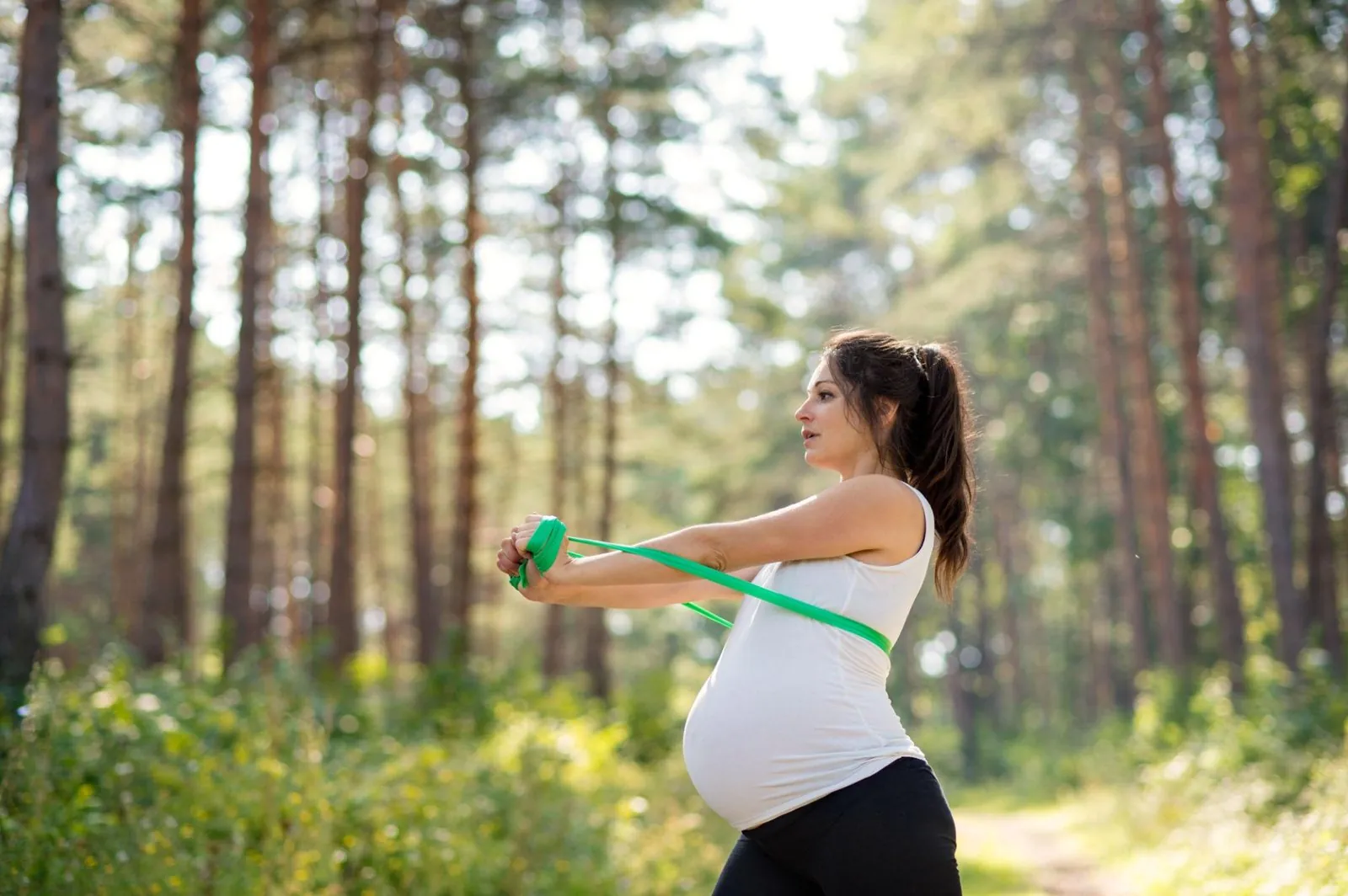 Zwangere vrouw traint buiten met een weerstandsband in het bos